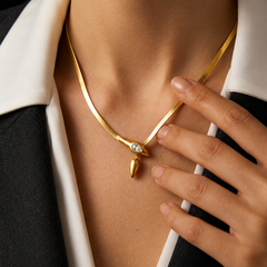 A close-up of a model wearing a gold snake-necklace with a small clear stone and teardrop pendant, styled with a black and white collared shirt.