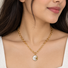 A close-up of a woman wearing a gold chain necklace with a circular pendant featuring a gold sunburst design on a white background.