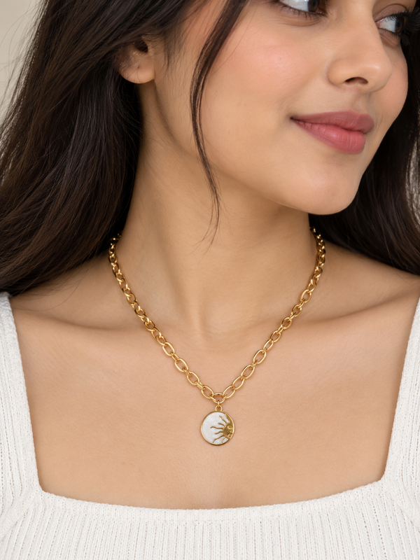 A close-up of a woman wearing a gold chain necklace with a circular pendant featuring a gold sunburst design on a white background.