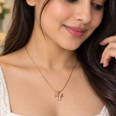 A woman wearing a delicate gold chain necklace with a small bow-shaped pendant adorned with pink and gold crystals, paired with a white lace top.