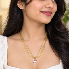 A woman wearing a layered gold necklace with a heart-shaped pink and white stone pendant, shown in a close-up portrait.