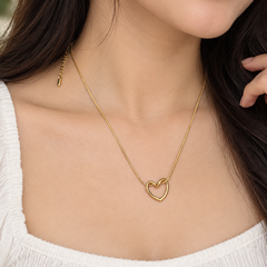 A close-up of a woman wearing a delicate gold chain necklace with an open heart pendant, styled with a white ribbed top.