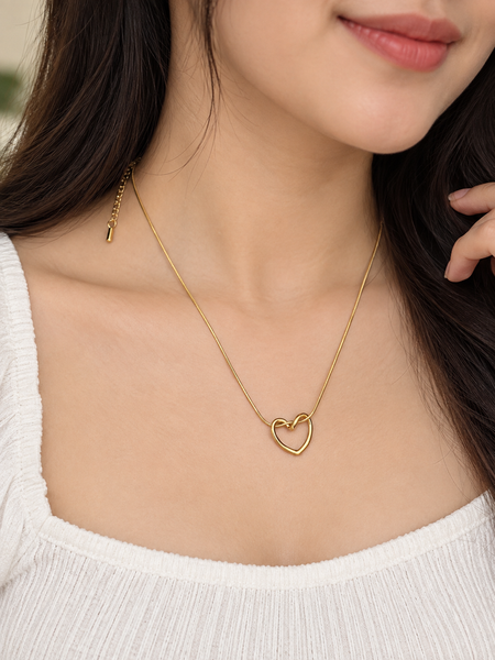 A close-up of a woman wearing a delicate gold chain necklace with an open heart pendant, styled with a white ribbed top.