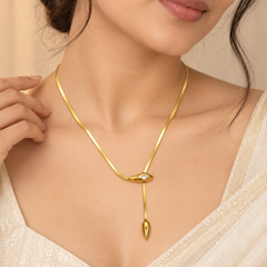 A close-up of a model wearing a delicate gold snake chain necklace with a unique pendant featuring a small clear stone and a teardrop-shaped drop.